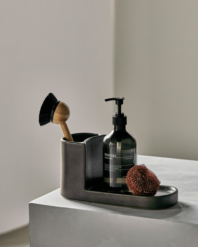 Meraki Datura brush and soap holder in dark grey stoneware, styled with a dish brush, soap bottle and scourer