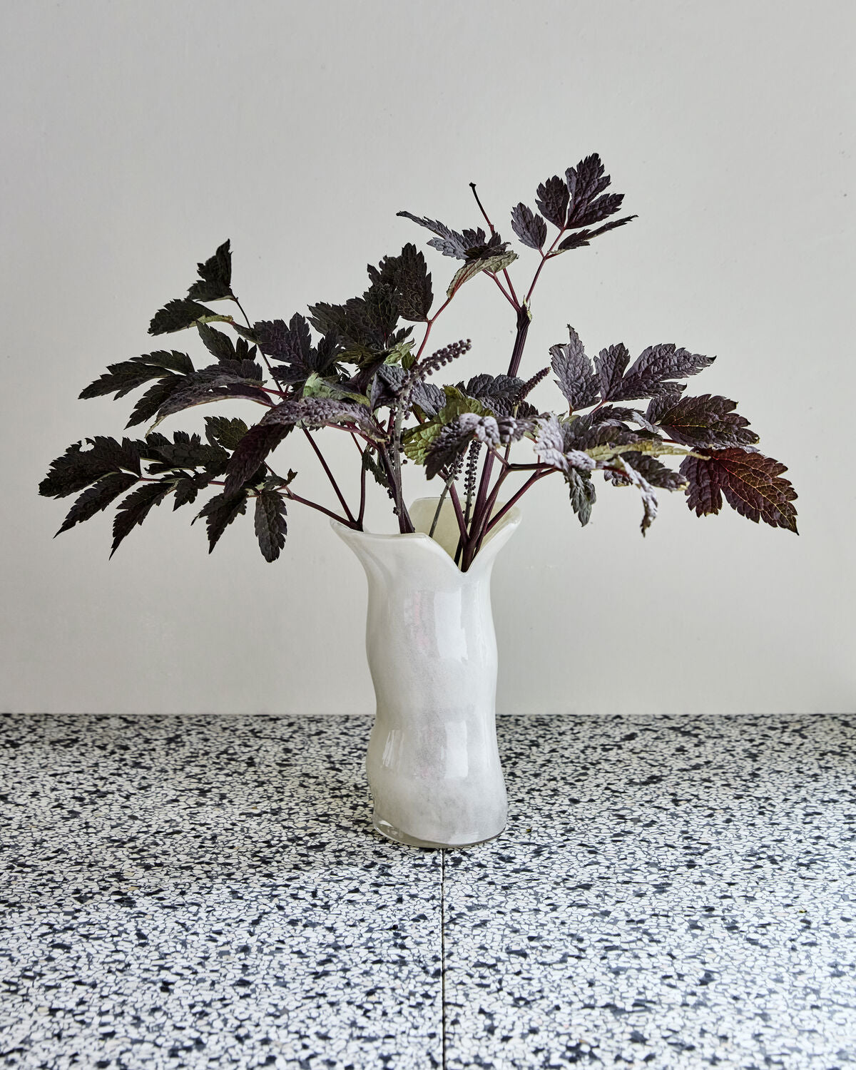 House Doctor Cuff off-white glass vase with dark foliage on a terrazzo surface