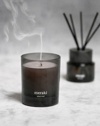 Meraki Velvet Mind candle burning with a trail of smoke, styled on a marble surface with a matching reed diffuser blurred in the background