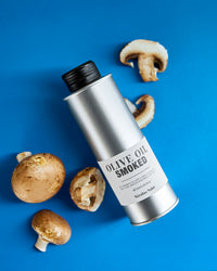 Nicolas Vahé Smoked Olive Oil tin styled on a blue background with fresh mushrooms