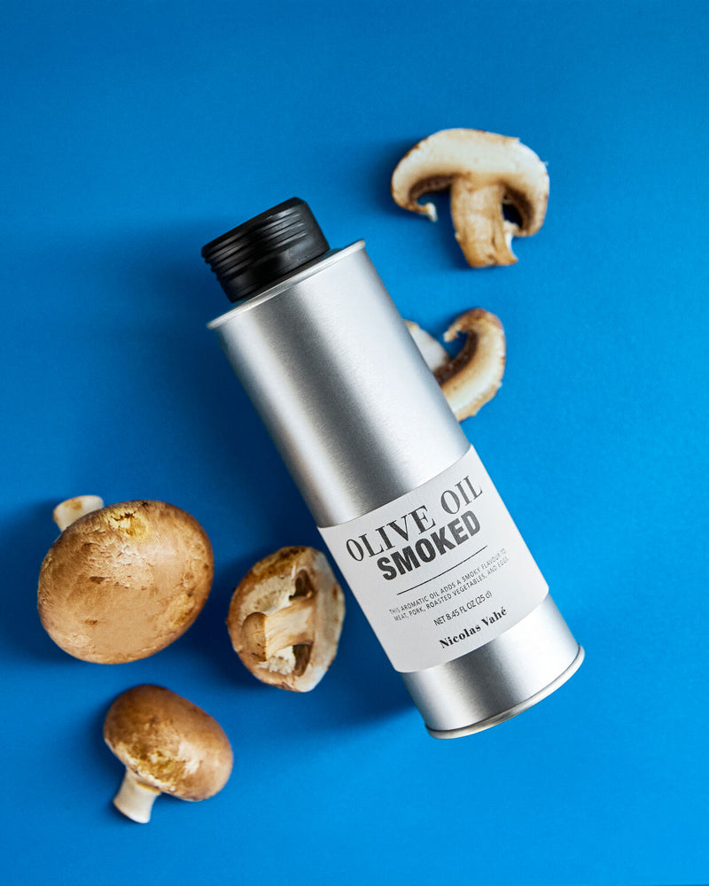 Nicolas Vahé Smoked Olive Oil tin styled on a blue background with fresh mushrooms