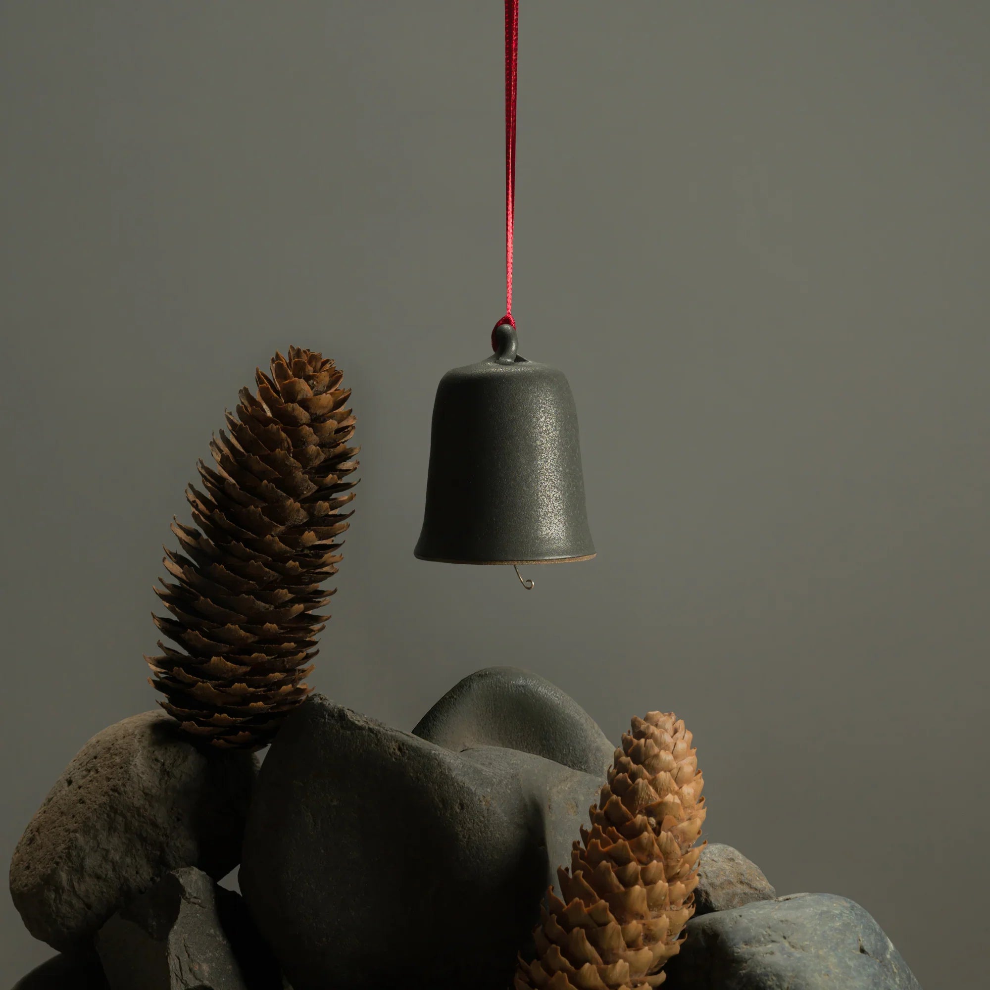 Fischersund JÓL limited edition holiday bell ornament hanging with pine cones in a moody winter scene