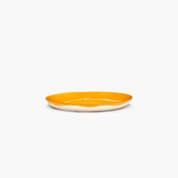 side of the yellow and white side plate from ottolenghi and serax showing the bright yellow pouring over half way down the lip bringing fun and joy to any dinnertable or party with friends