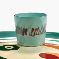 azure blue with red striped espresso cup on a plate with handpainted face in ottolenghi's indomnitable style