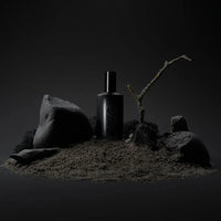 a black bottle of flotholt perfume stood on a sandy hill with black rocks around it