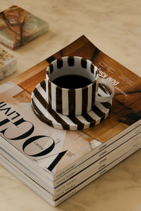 Monica brown striped cup and saucer by Olsson & Jensen with coffee on a stack of magazines