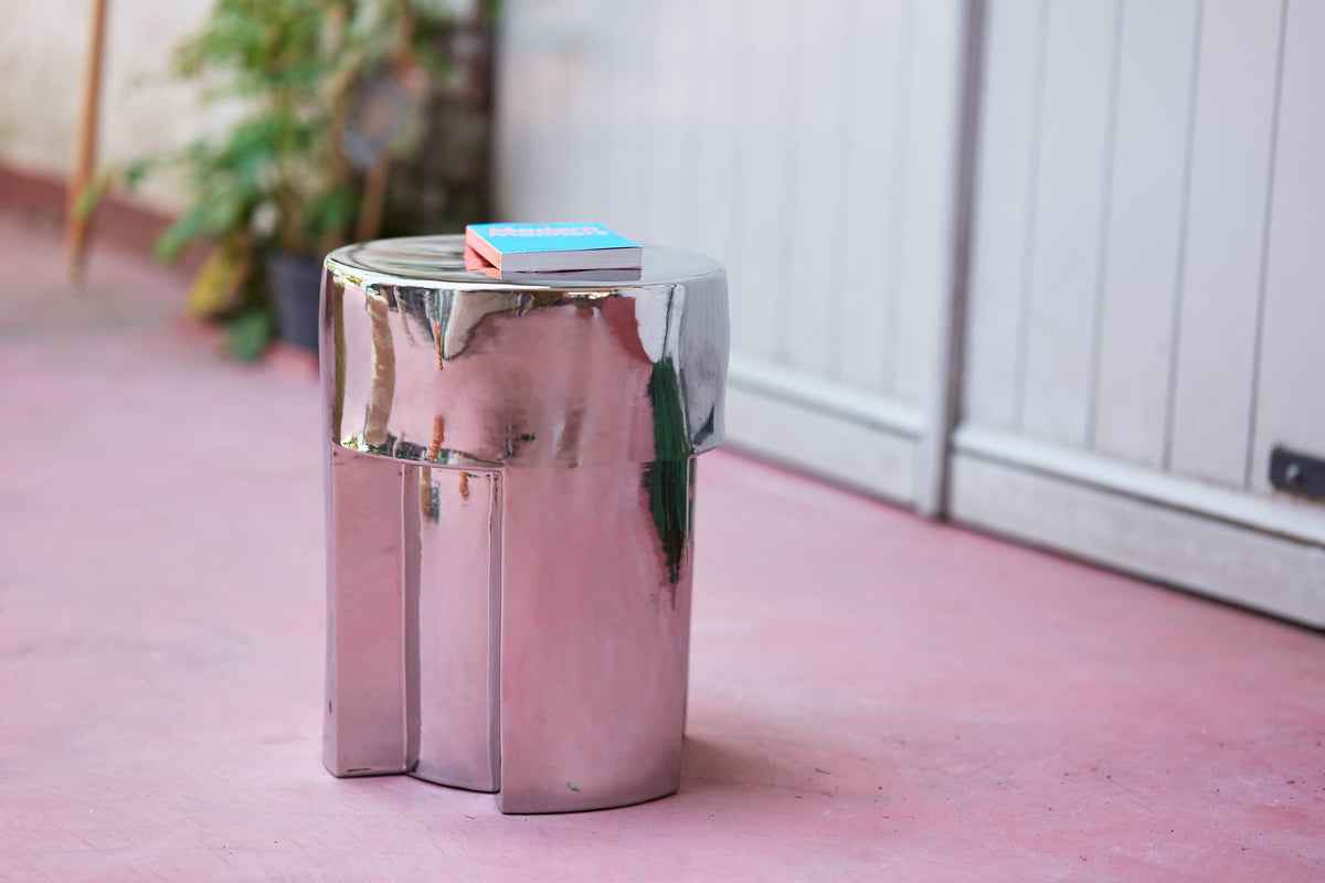 Chrome HKLIVING stoneware side table with books on top on a pink floor beside a plant