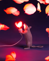 Seletti Pink Mouse Lamp with a glowing red heart bulb among red petals