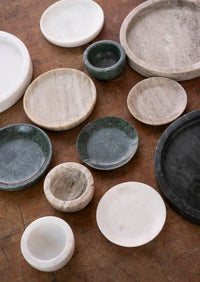 assorted marble trays and small bowls in beige white and green tones on a wooden surface
