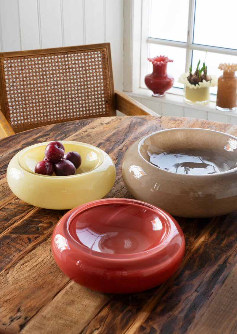 taupe glass bowl styled with yellow and red bowls on wooden table

