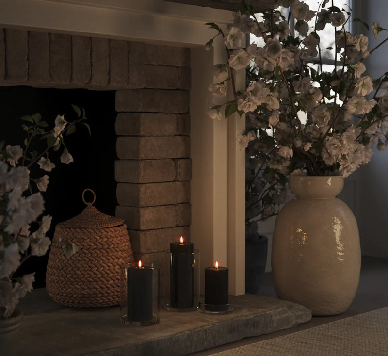 set of black LED pillar candles glowing warmly in glass holders on a stone fireplace