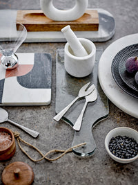 soft grey marble cutting board by bloomville styled with utensils and serving bowls on a textured stone surface
