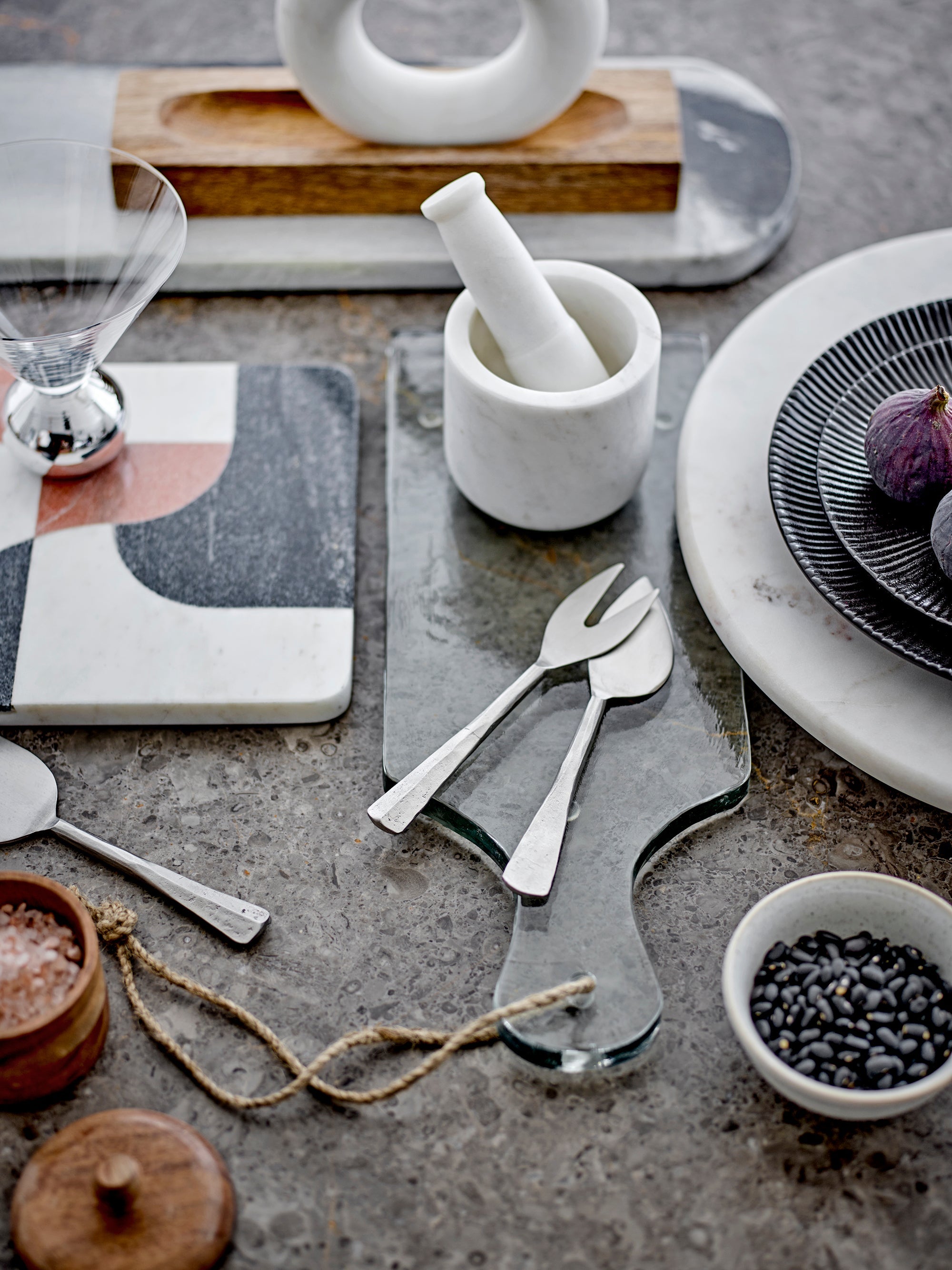 soft grey marble cutting board by bloomville styled with utensils and serving bowls on a textured stone surface
