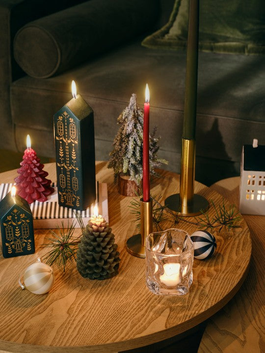 Lit dark green Casa house candles with a red tree candle, pine cone candle and brass candlesticks on a wooden coffee table