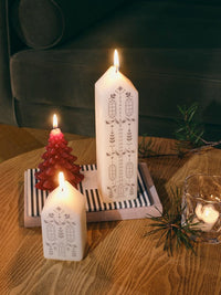 Lit white Casa house candles with a red tree candle on a striped tray on a wooden table