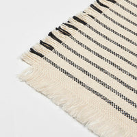 Close-up of the Elouise coaster showing the woven black stripes and fringed edge
