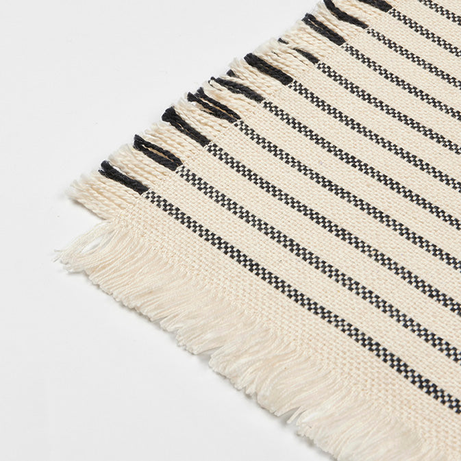Close-up of the Elouise coaster showing the woven black stripes and fringed edge