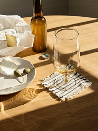 Elouise striped cotton coaster under a glass on a sunlit wooden dining table
