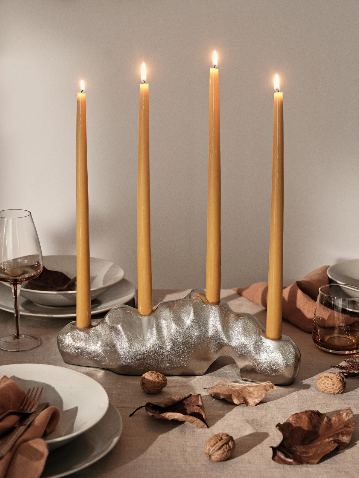 Golden yellow glossy taper candles lit in a silver sculptural holder on a set dining table