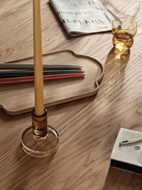 Close-up of a golden yellow glossy taper candle in an amber glass holder on a wooden table