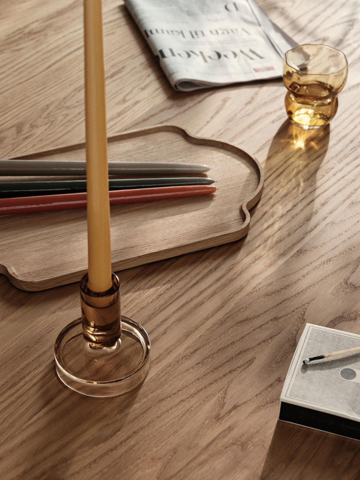 Close-up of a golden yellow glossy taper candle in an amber glass holder on a wooden table