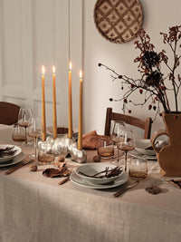 Golden yellow taper candles on a dining table dressed with dried branches and stoneware