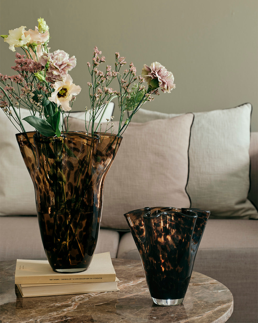 Large and small Liva vases in brown leopard glass with pale pink flowers on a marble coffee table