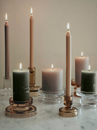 Group of Petra glass holders with green and grey pillar candles and tall tapers on a marble table
