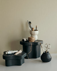 Low and tall black Sonja pedestals styled with ceramics and a vase against a pale wall
