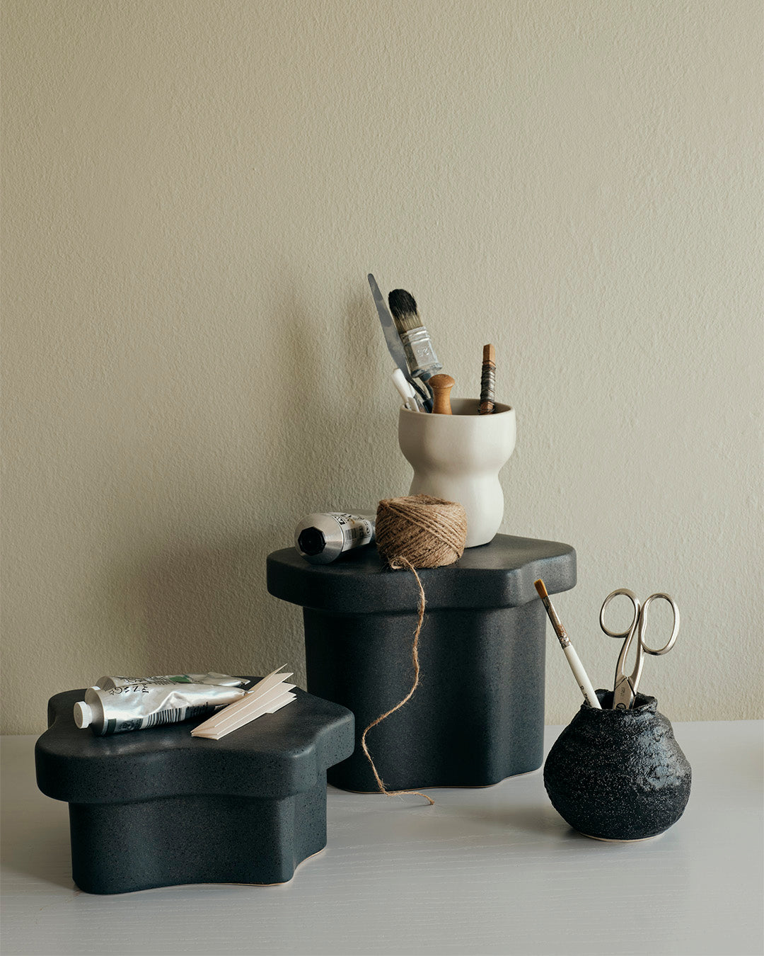 Low and tall black Sonja pedestals styled with ceramics and a vase against a pale wall
