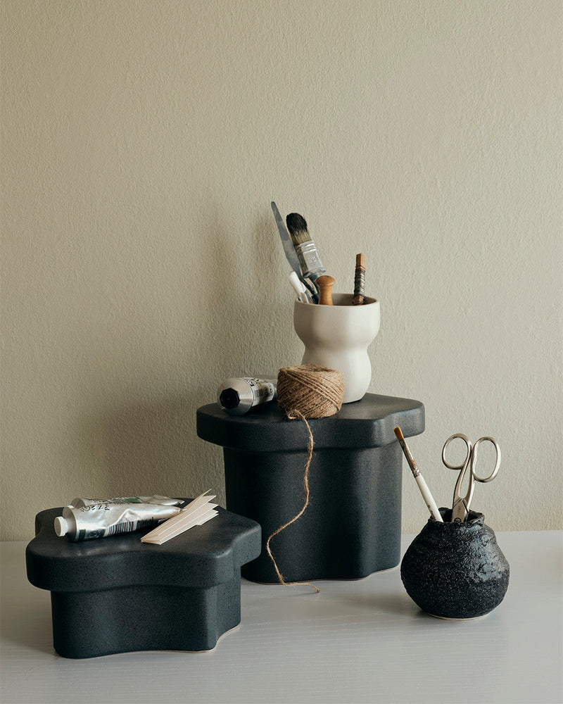 Low and tall black Sonja pedestals styled with ceramics and a vase against a pale wall