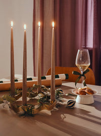 Lit taupe glossy taper candles on a festive table with wrapped gifts and a glass of wine