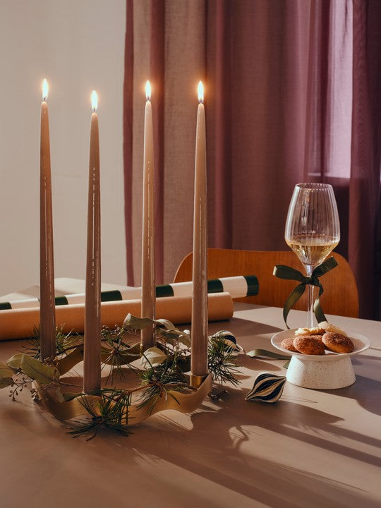 Lit taupe glossy taper candles on a festive table with wrapped gifts and a glass of wine