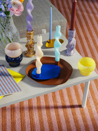 Thin taper candles in colourful wavy holders on a white table with a striped rug
