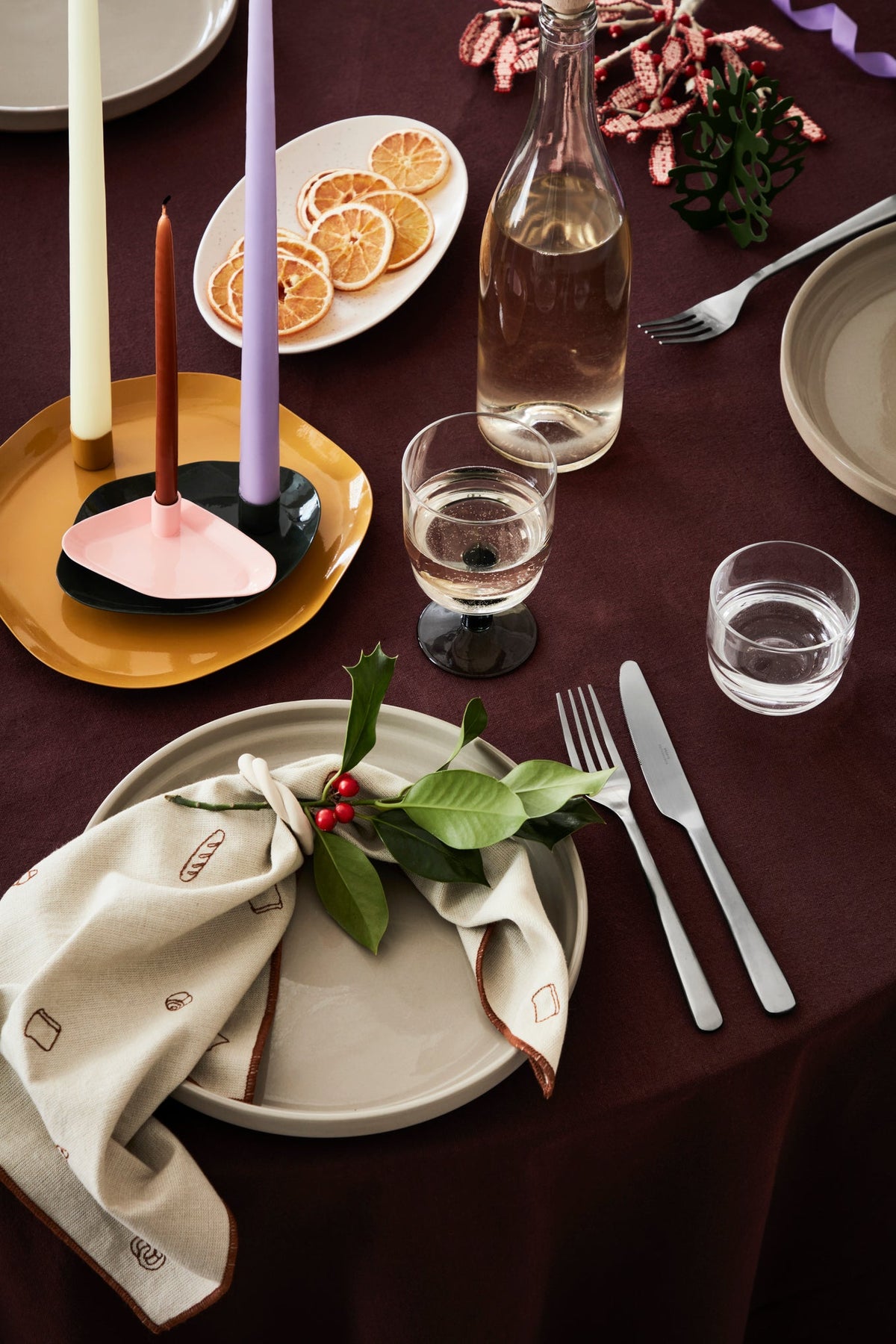 Thin taper candles in sculptural holders on a festive dinner table with a burgundy tablecloth