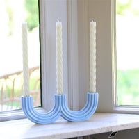 Light blue Churros candle holder with two cream taper candles on a sunny windowsill