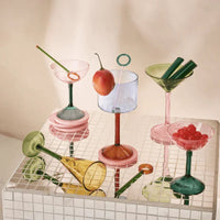 Colourful cocktail glasses including the rose pink coupe styled with fruit on a tiled surface