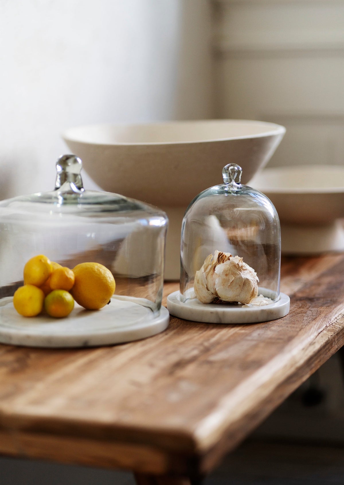 small glass cloches with marble bases displaying lemons and garlic on wooden table