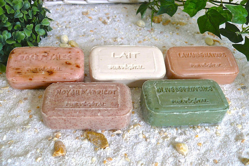 Assorted handmade French vegetable soaps on sand, including Milk fragrance bar