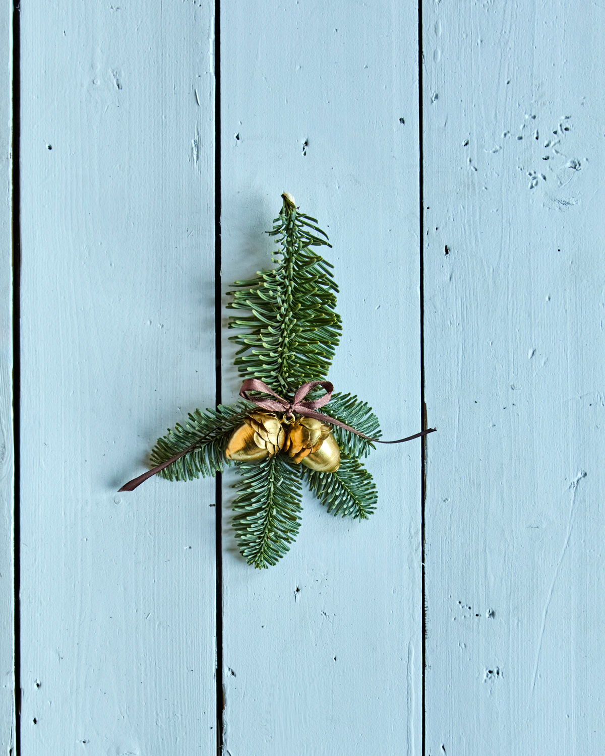 House Doctor gold acorn decorations tied to a pine sprig on a pale blue painted wooden door