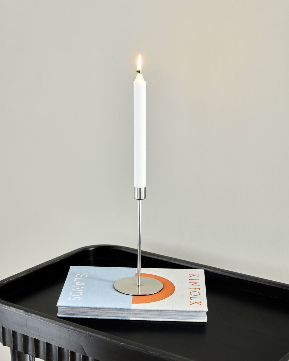 Tall House Doctor Anit candle holder in brushed silver with a lit white candle on a black side table