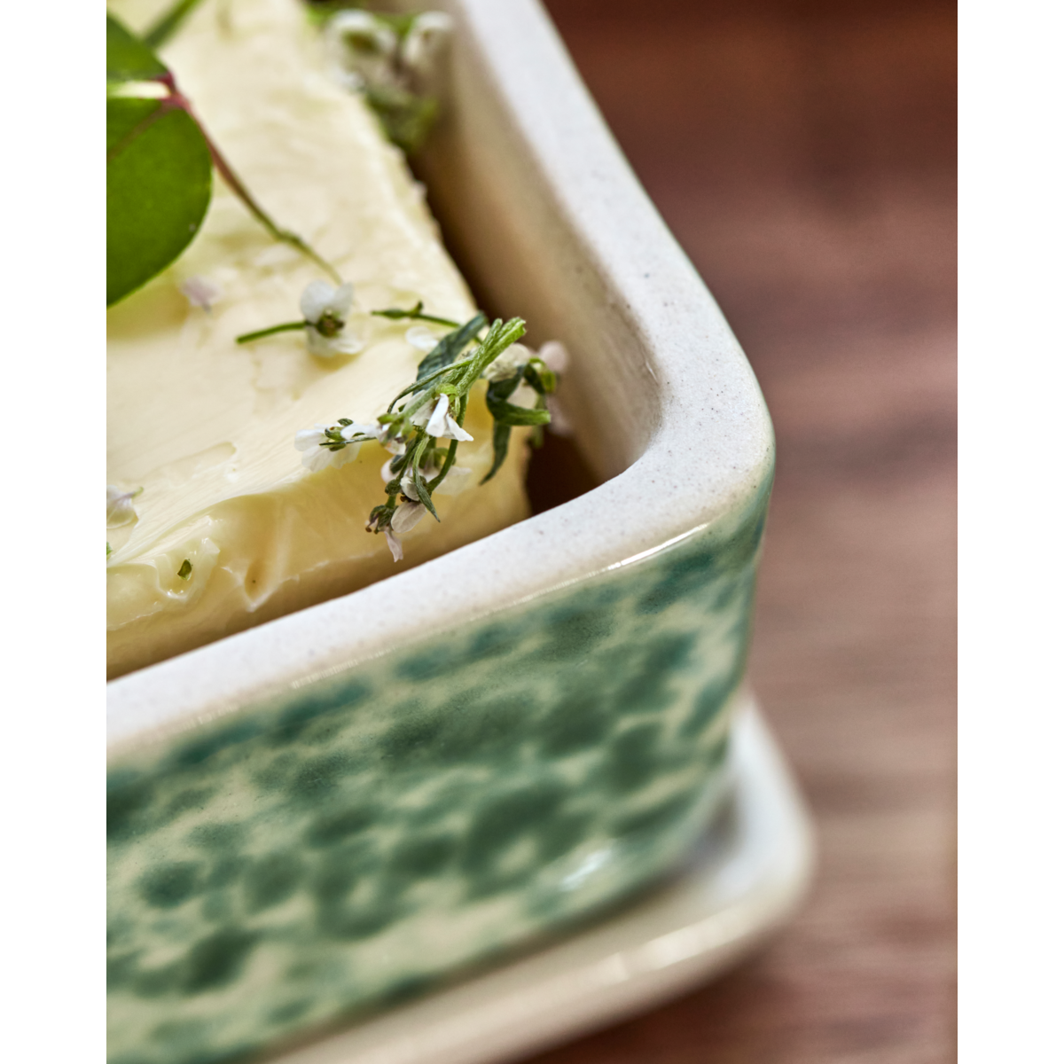 Close-up of green ceramic butter dish with herb garnish
