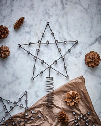 House Doctor Connect star tree topper on marble with pine cones and brown wrapping paper