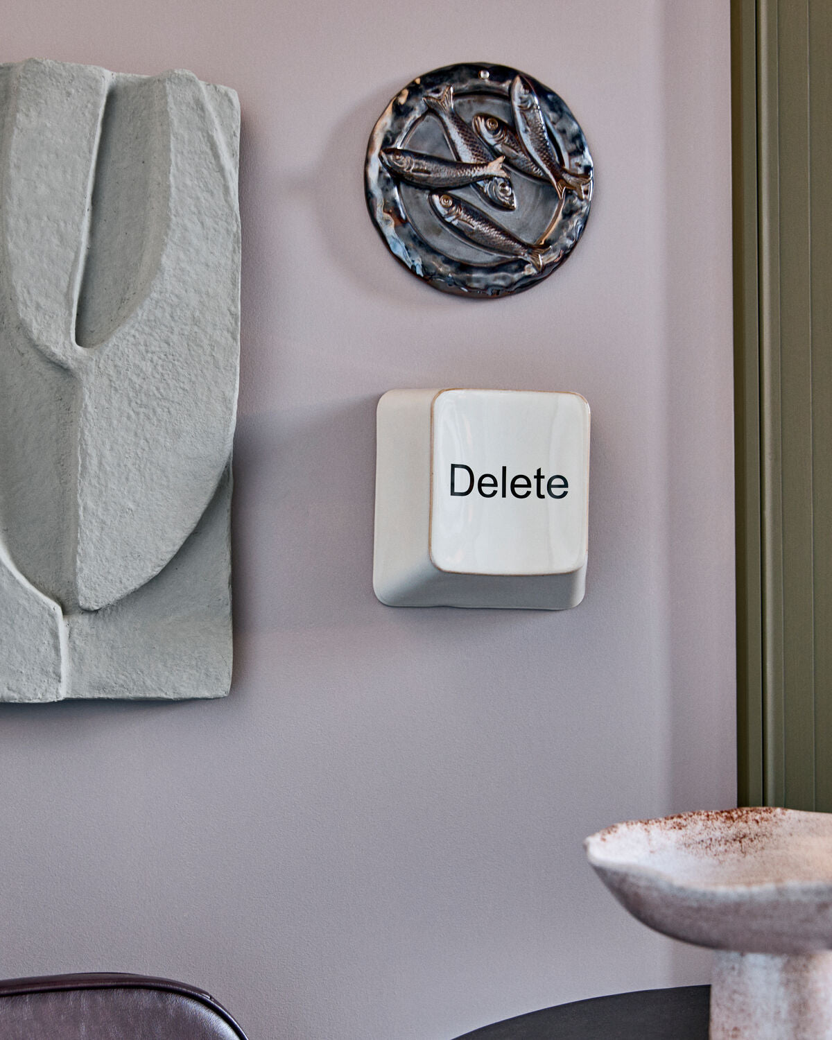 House Doctor Delete key ceramic wall art hung on a lilac wall with other ceramic wall pieces
