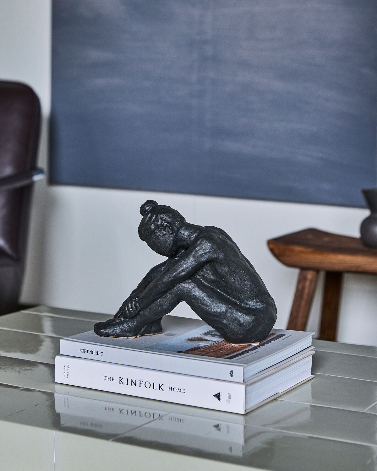 House Doctor Forms black seated figure sculpture on books on a glass table in a dark living room