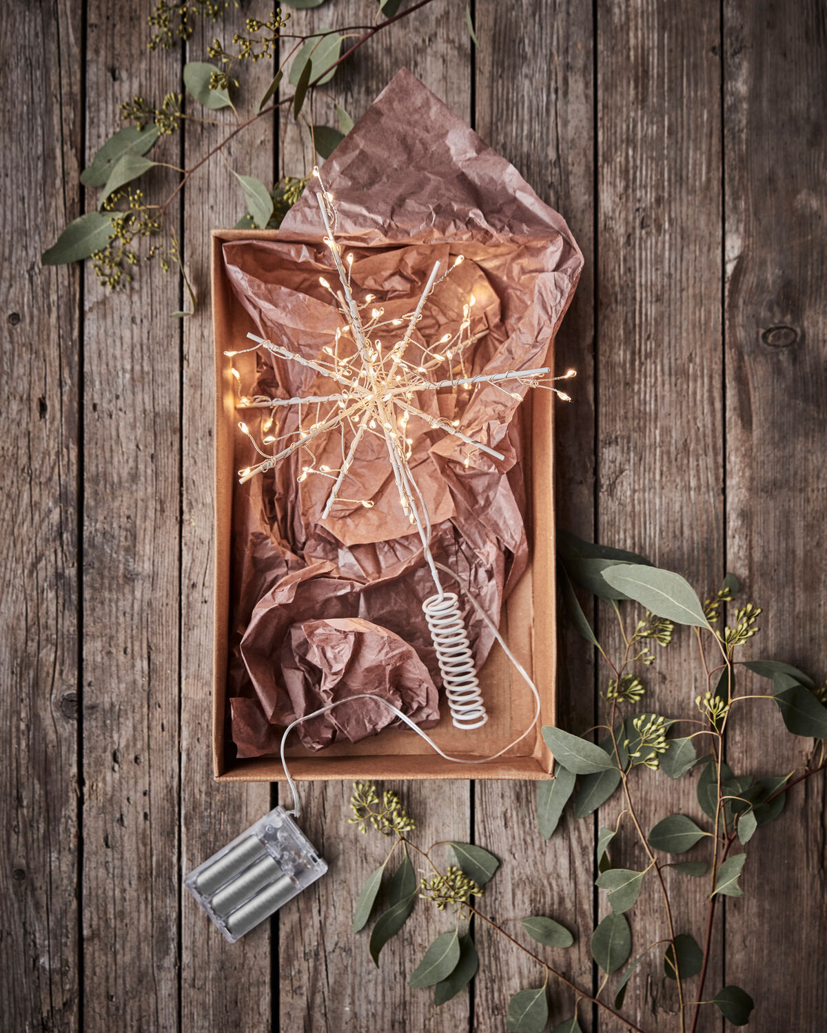 House Doctor Glow LED starburst tree topper lit in a wooden tray with brown paper and greenery