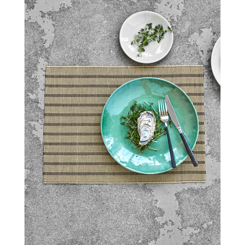 Placemat styled with green plate and cutlery on concrete surface
