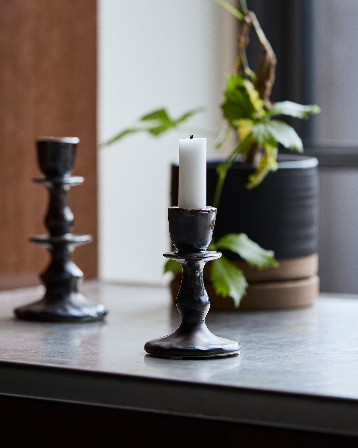 House Doctor Lucca candle holders in Black, styled together in two heights on a tabletop with a candle and a potted plant
