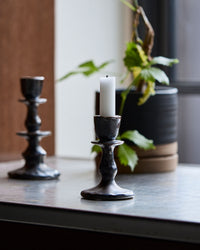 House Doctor Lucca candle holders in Black, styled together in two heights on a tabletop with a candle and a potted plant