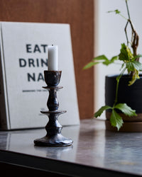 House Doctor Lucca Candle Holder, Black, Large, styled with a lit candle next to a book and a potted plant